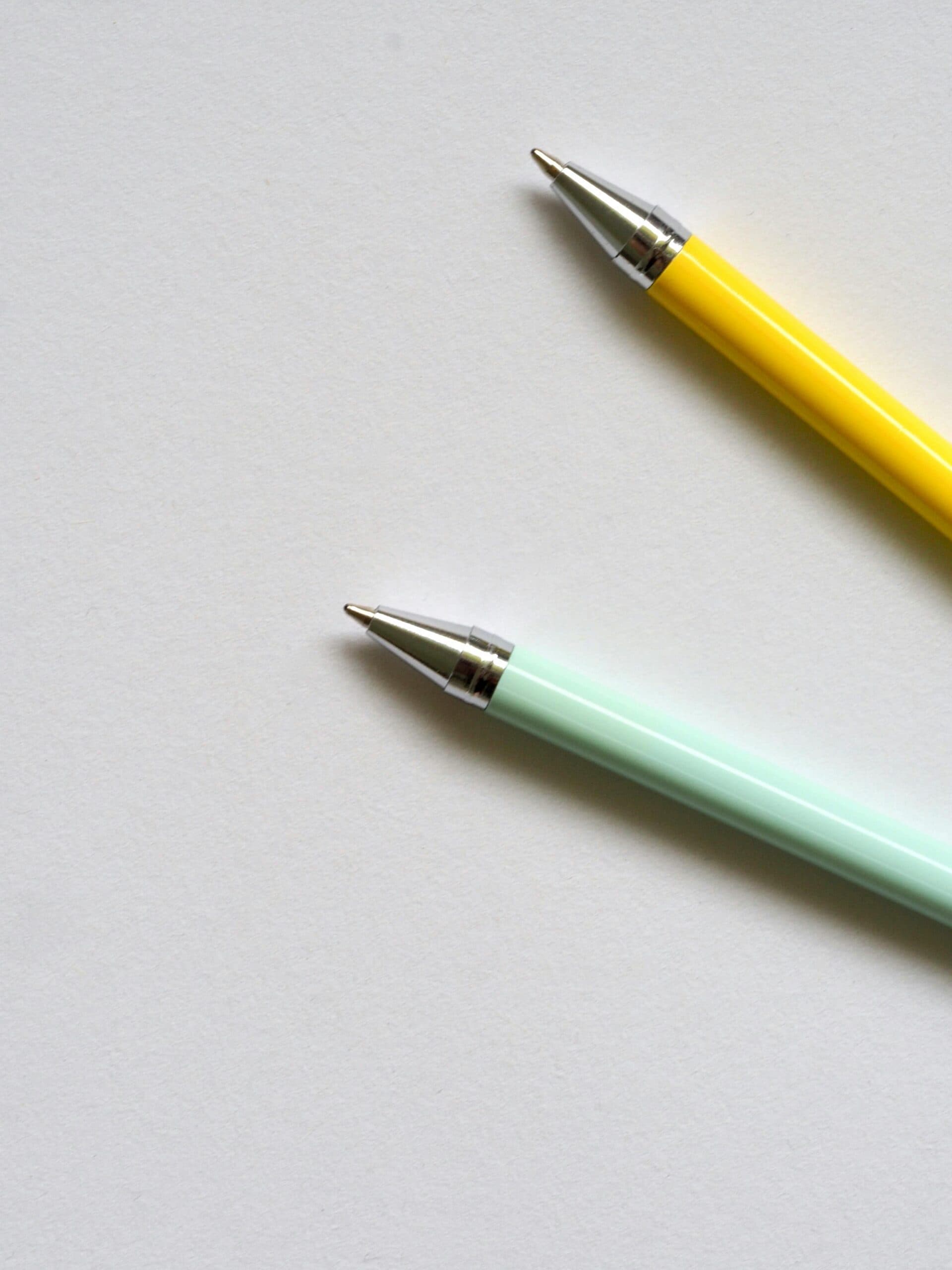 Minimalist shot of two colorful ballpoint pens on a plain white surface. Perfect for office or school themes.